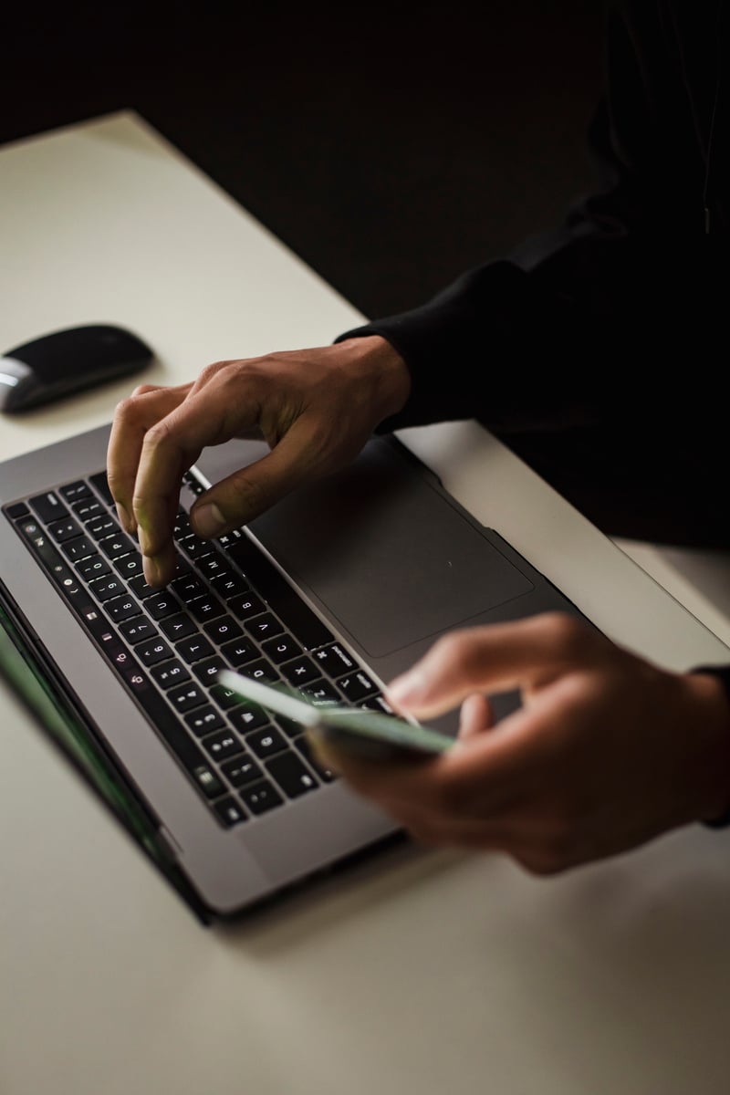 Crop faceless man using laptop and smartphone in office